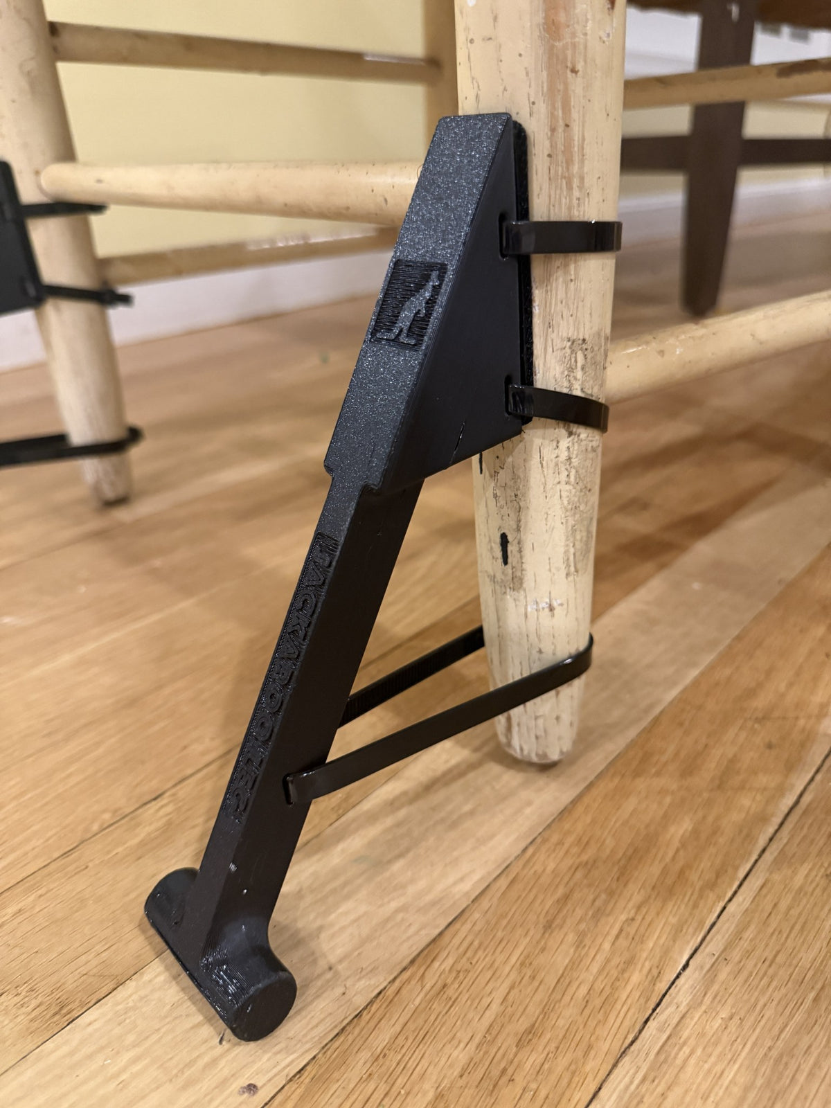 Close-up of the new Jackaroo Leg chair stabilizer attached to a wooden chair leg with straps to stop the chair tipping backwards